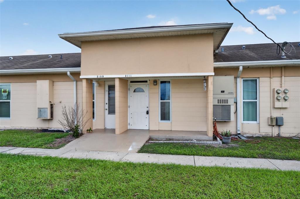 A single-story duplex building with tan exterior walls, two front doors, and a shared porch — 3111 CLUB CIRCLE, LAKE WALES, FL