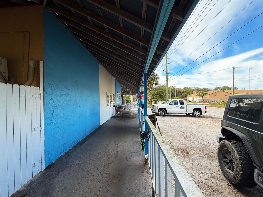 A covered walkway runs alongside a blue building with a white fence and parked vehicles — 6028 PINE HILL ROAD, PORT RICHEY, FL