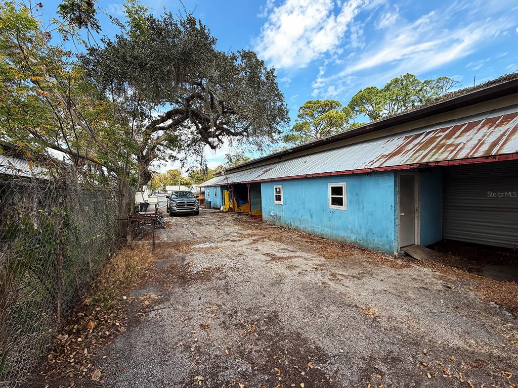 An exterior view of a blue, single-story building with a metal roof and gravel lot — 6028 PINE HILL ROAD, PORT RICHEY, FL