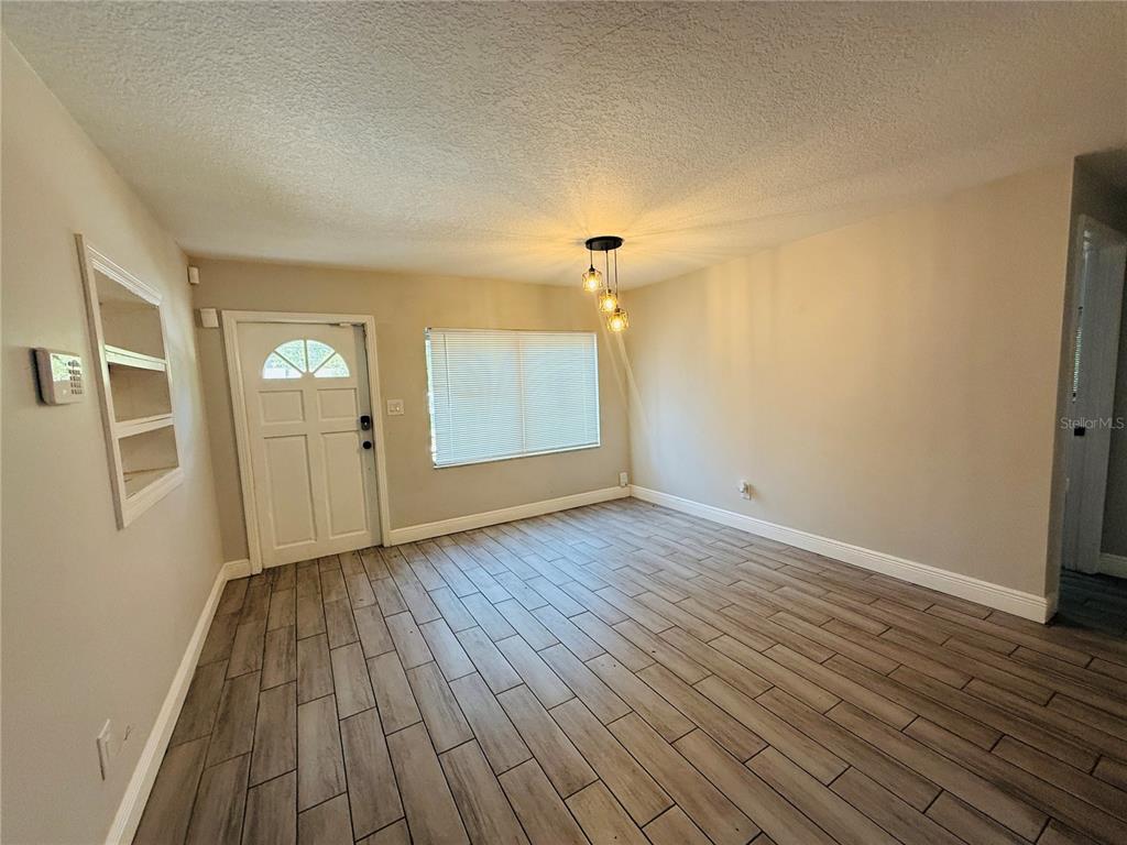 An empty room features wood-look tile flooring, a front door, a window, and pendant lighting — 4203 E YUKON STREET, TAMPA, FL