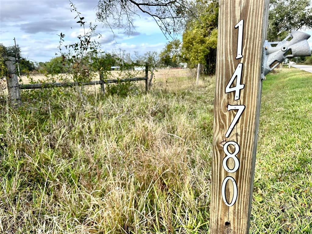 A wooden post displays the house number 14780 next to a rural field and fence — 14780 SUGAR BOWL ROAD, MYAKKA CITY, FL