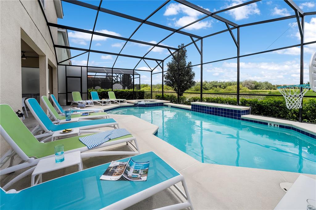 A screened-in swimming pool with lounge chairs on a patio overlooking a grassy field — 8009 OAK SHADOW COURT, DAVENPORT, FL