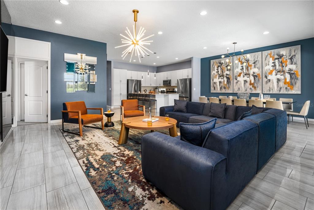 A modern open-concept living and dining area features blue walls, a large sectional, and tile flooring — 8009 OAK SHADOW COURT, DAVENPORT, FL