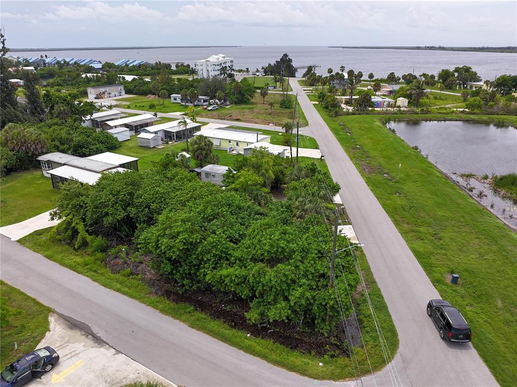 An aerial view shows a residential street with mobile homes, lush vegetation, and a nearby pond — 4572 STURKIE AVENUE, PORT CHARLOTTE, FL
