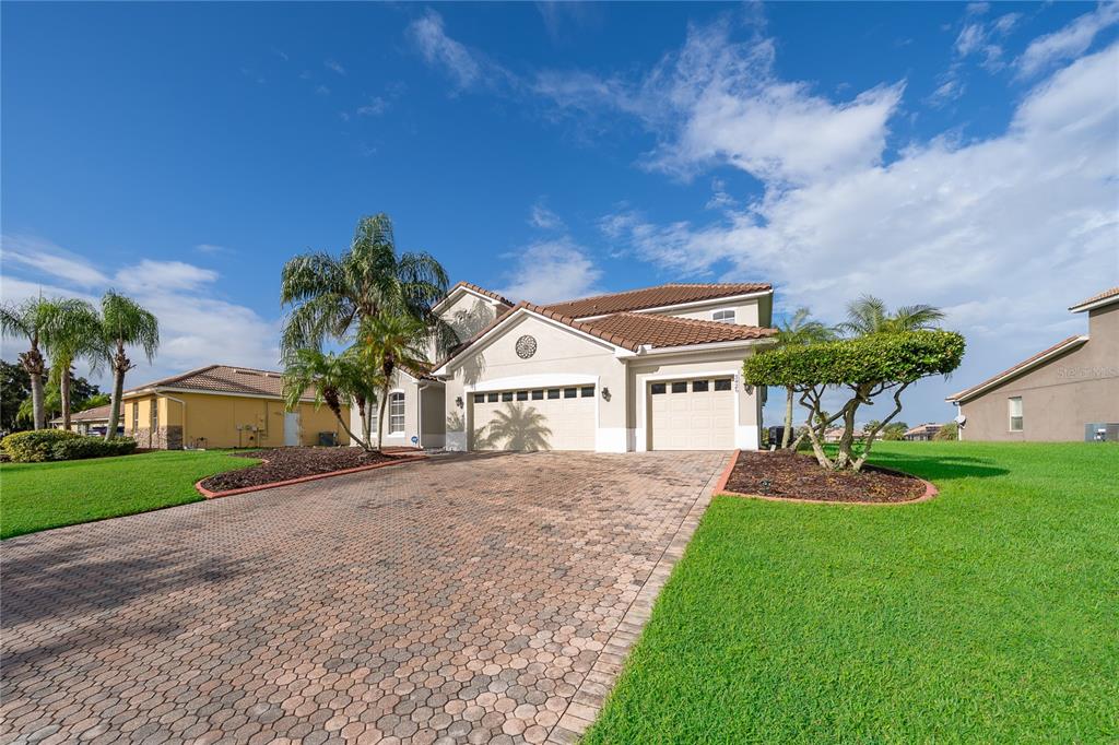 A two-story house with a paved driveway, three-car garage, and palm trees under a blue sky — 3426 HARBORSIDE COURT, KISSIMMEE, FL