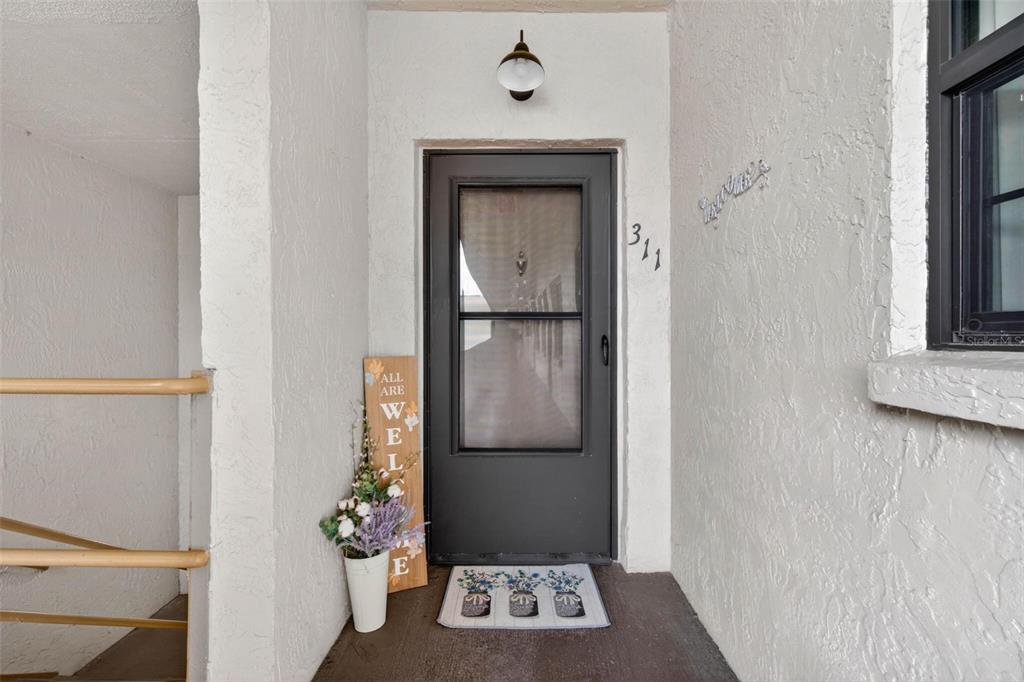 A front entryway features a dark storm door, a welcome sign, and a floor mat — 5975 TERRACE PARK DRIVE N UNIT 311, ST PETERSBURG, FL