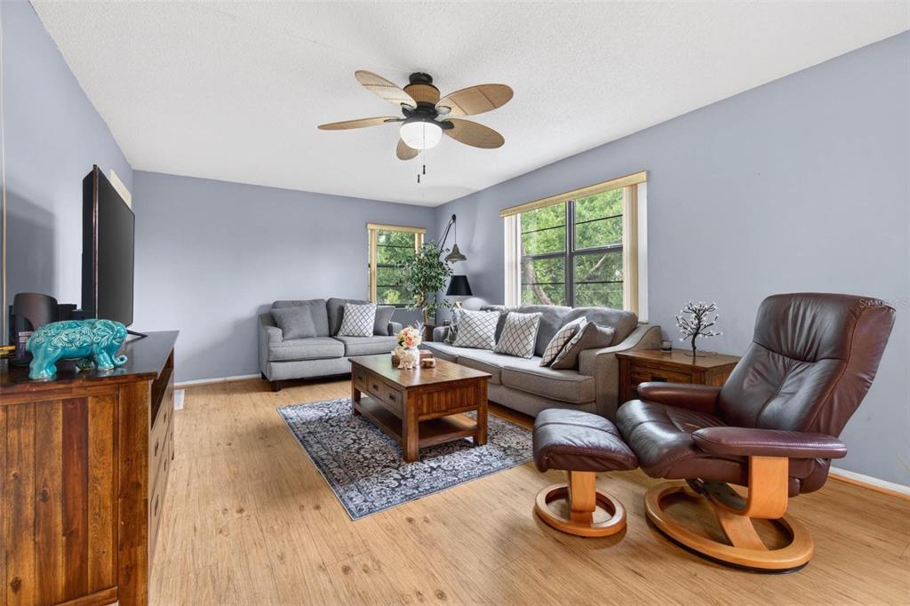 A living room with light blue walls, wood-look flooring, gray sofas, and a leather recliner — 5975 TERRACE PARK DRIVE N UNIT 311, ST PETERSBURG, FL
