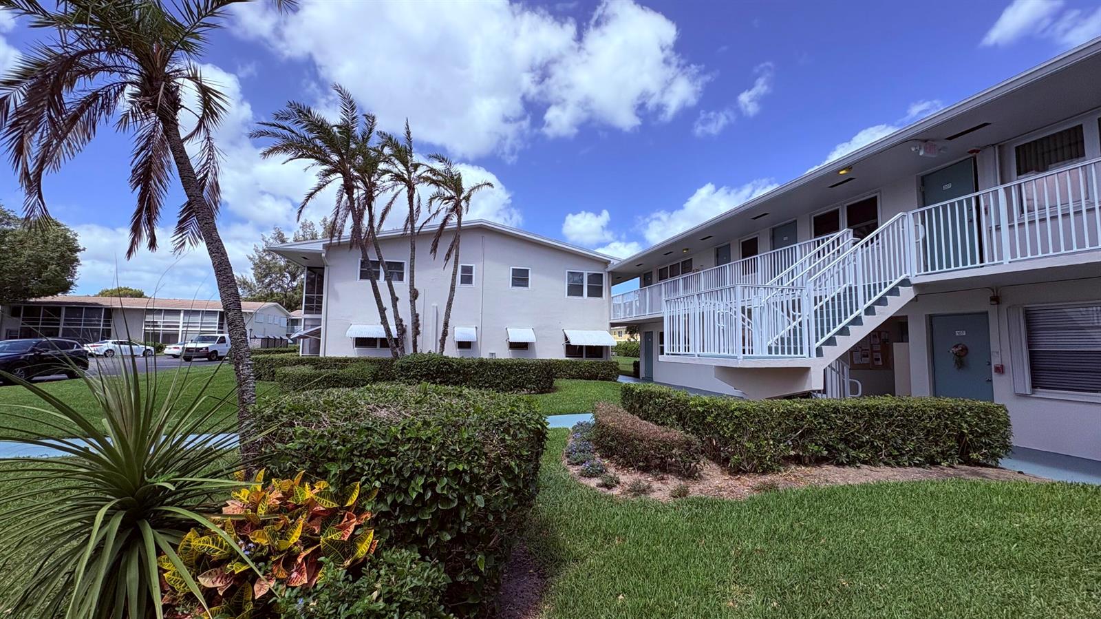 Exterior view of a two-story apartment complex with palm trees and a landscaped lawn — 200 Horizon W # 102, Boynton Beach FL 33435, BOYNTON BEACH, FL