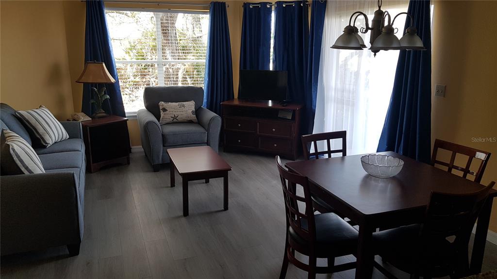 A living and dining area features blue curtains, wood-look flooring, and a dark wood table — 6403 PARC CORNICHE DRIVE UNIT 4107, ORLANDO, FL