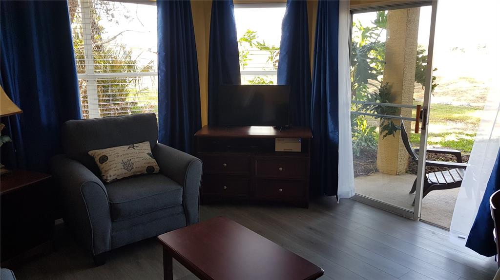 A living room features a gray armchair, a television on a dresser, and a sliding door — 6403 PARC CORNICHE DRIVE UNIT 4107, ORLANDO, FL