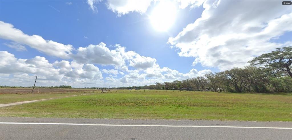 A wide, grassy vacant lot sits alongside a paved road under a bright, cloudy sky — COMMONWEALTH AVE N, POLK CITY, FL