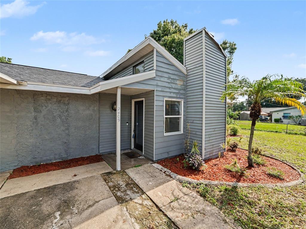 A gray house exterior features horizontal siding, a covered entryway, and a small front yard — 2409 11TH AVENUE SE, RUSKIN, FL