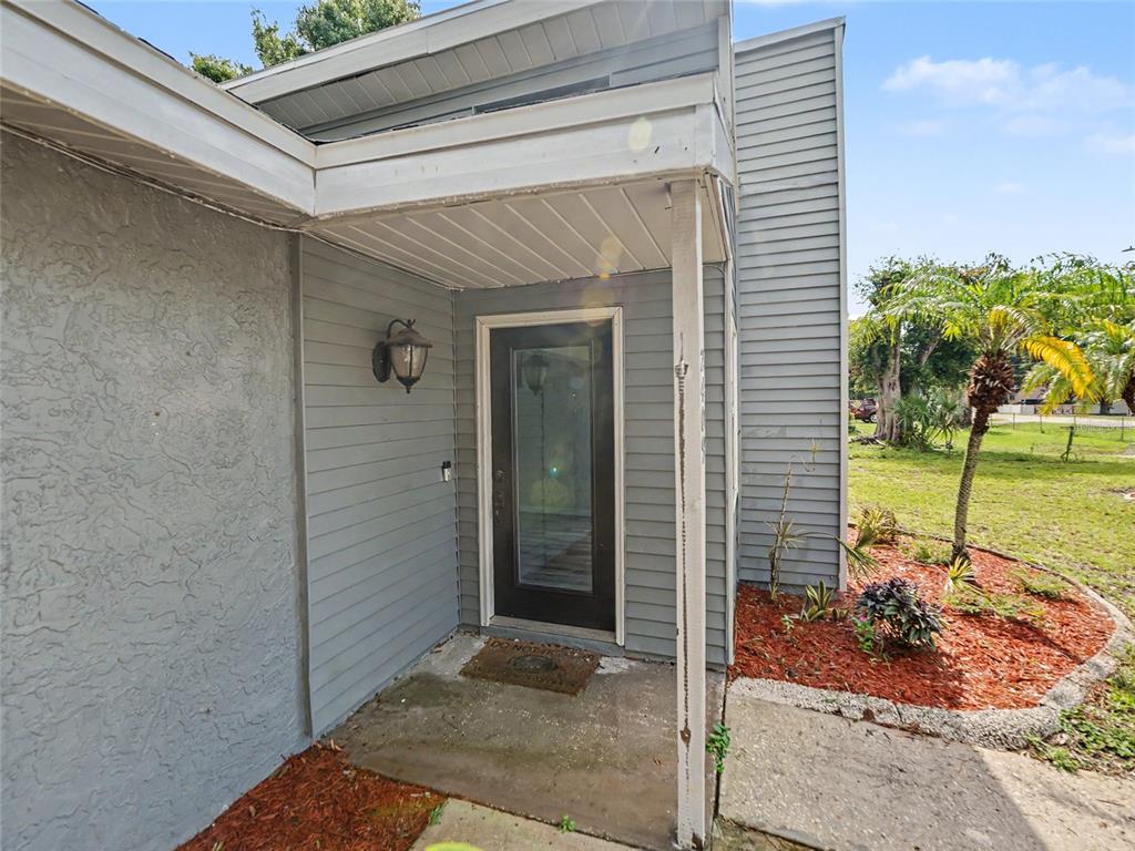 The exterior entrance features a gray siding facade, a dark glass door, and a porch — 2409 11TH AVENUE SE, RUSKIN, FL