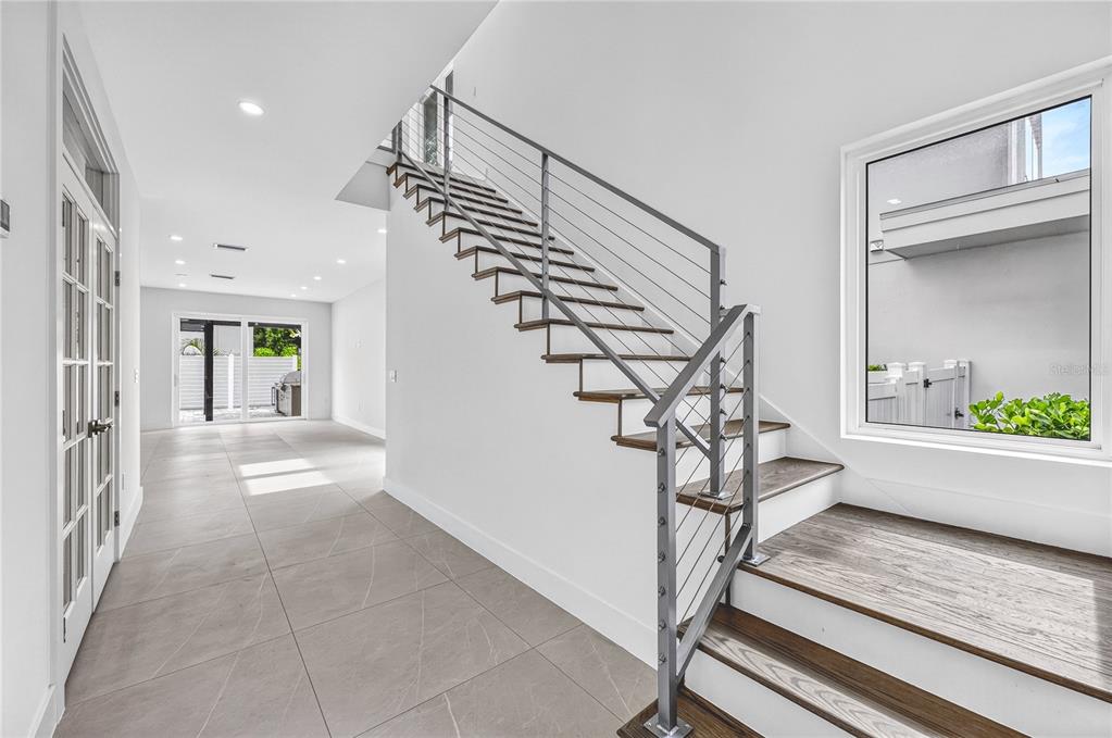 A modern entryway features a floating staircase with cable railings and large-format tile flooring — 2590 FLOYD STREET, SARASOTA, FL