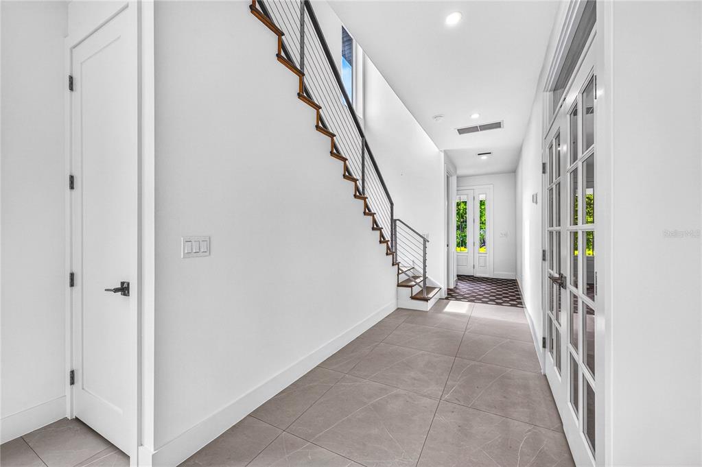 A modern hallway features large gray floor tiles, a staircase with cable railings, and French doors — 2590 FLOYD STREET, SARASOTA, FL