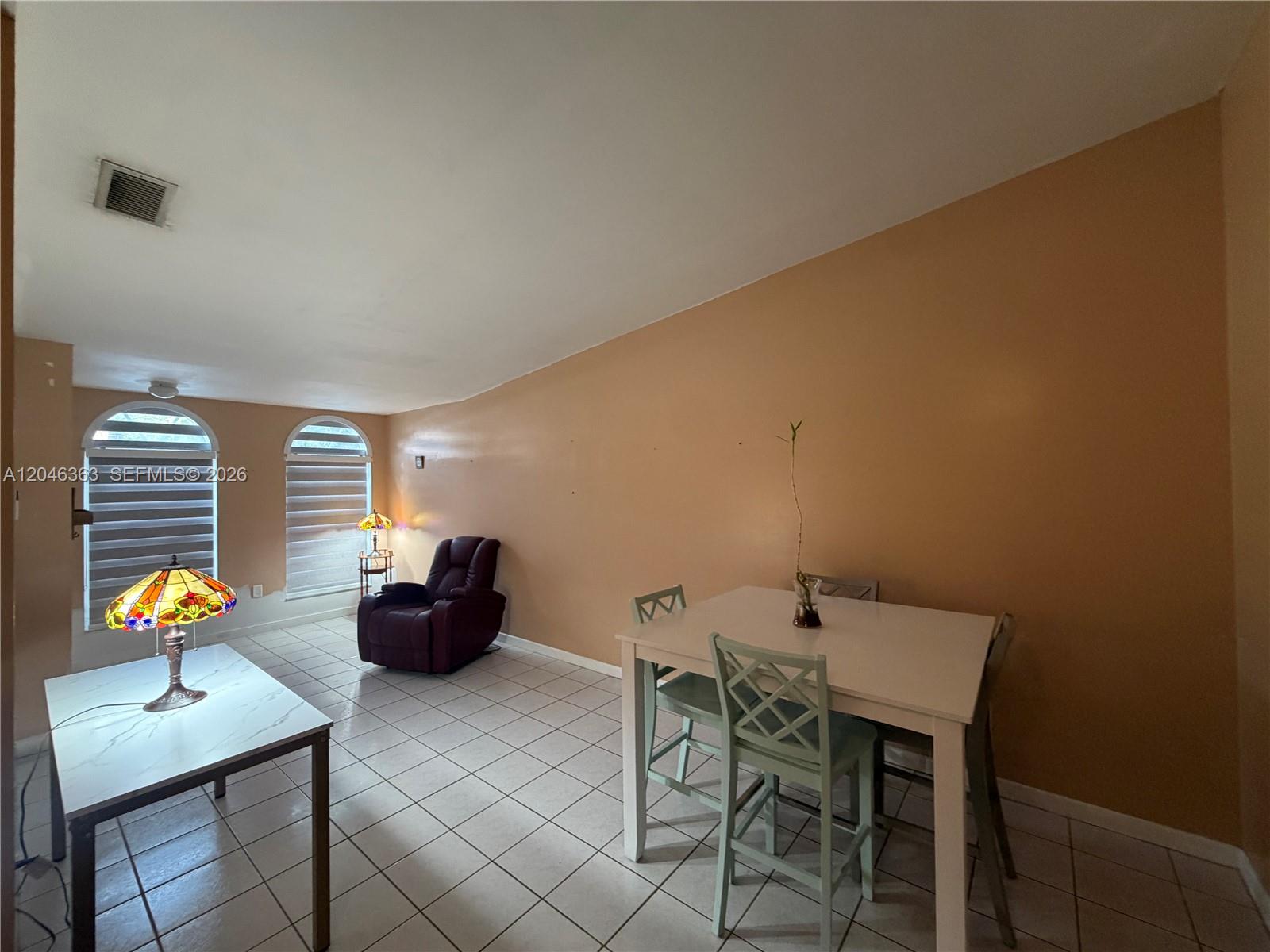 A dining area with tile floors, a white table, and a recliner near arched windows — 6718 NW 166th Ter # 301, Miami Lakes FL 33014, MIAMI LAKES, FL