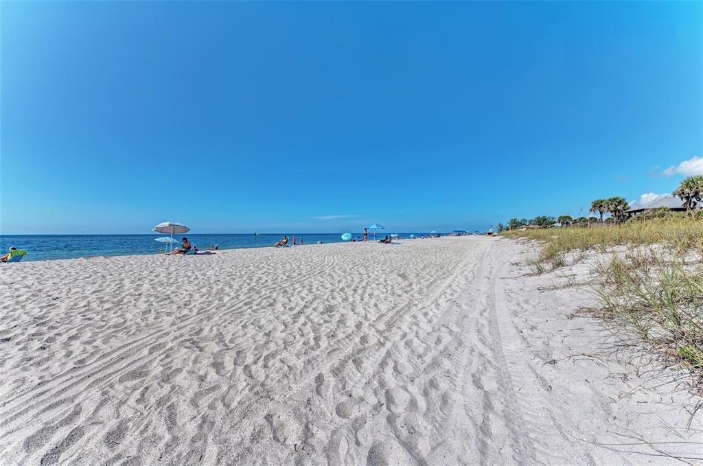 A wide, sandy beach with umbrellas and dunes under a clear blue sky — 7383 TALLEY STREET, PORT CHARLOTTE, FL