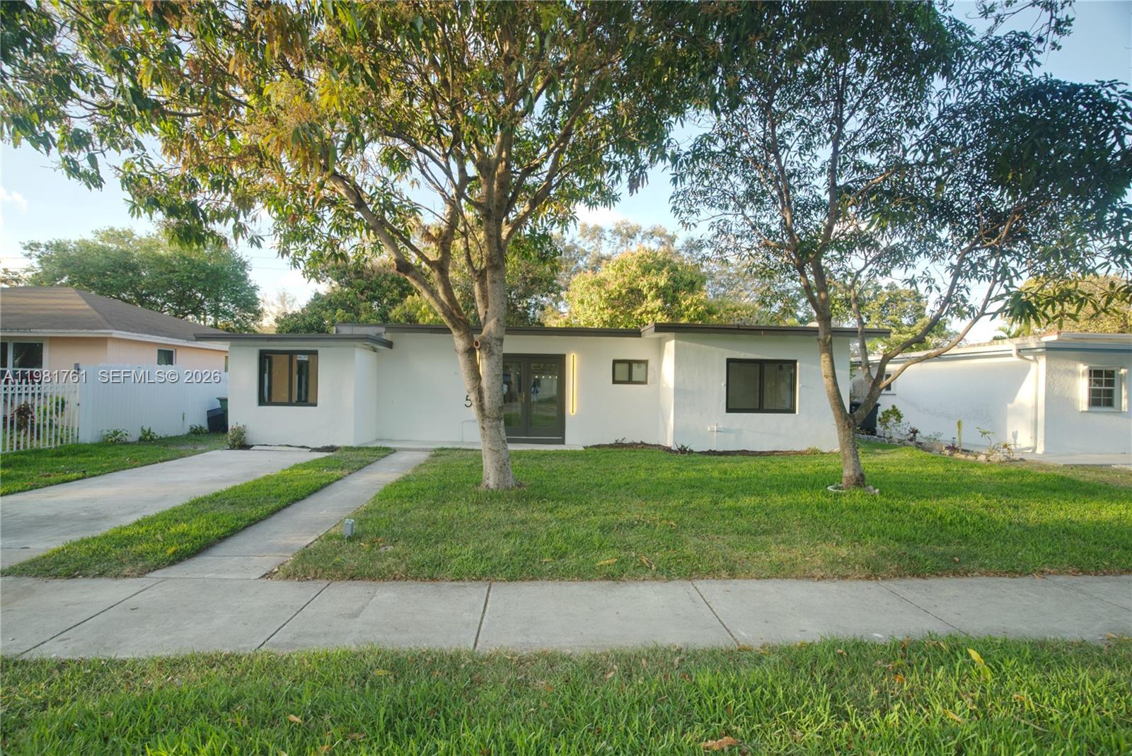 A single-story white house with a flat roof, dark-framed windows, and two large trees — 315 NW 127th St, North Miami FL 33168, NORTH MIAMI, FL