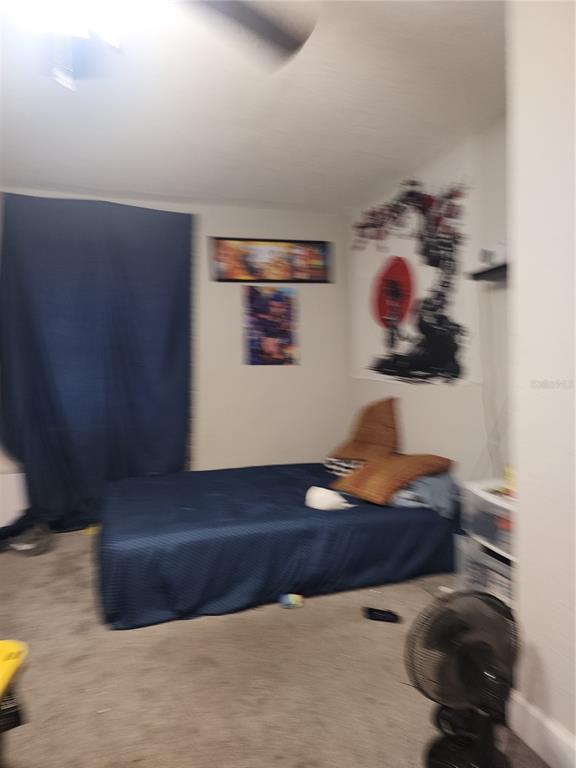 A bedroom features a blue bed, dark curtains, wall art, and a portable fan — 2439 LAKEVIEW STREET, LAKELAND, FL