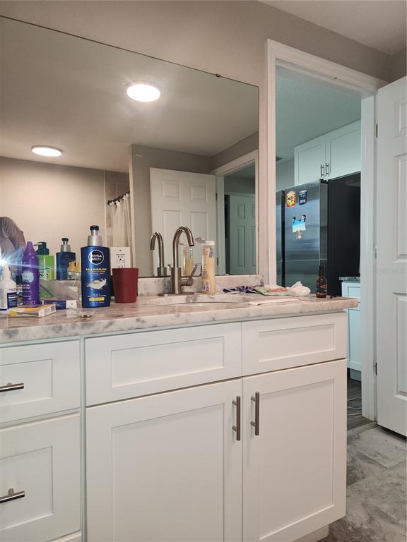A bathroom vanity with a marble countertop, white cabinets, and a mirror, looking toward a kitchen — 2439 LAKEVIEW STREET, LAKELAND, FL
