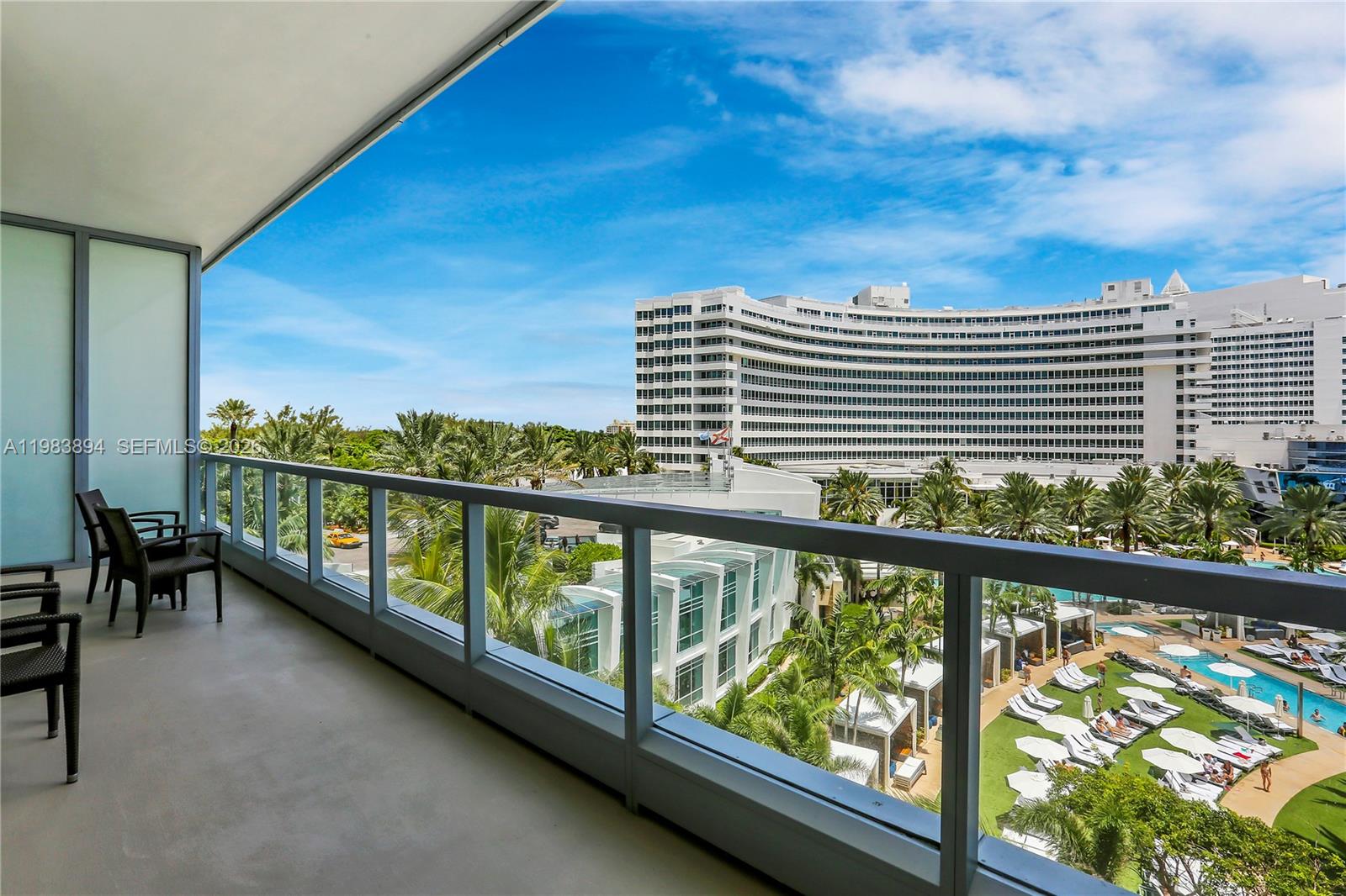 A balcony with outdoor seating overlooks a resort pool area and a large curved building — 4391 Collins Ave, Miami Beach FL 33140, MIAMI BEACH, FL