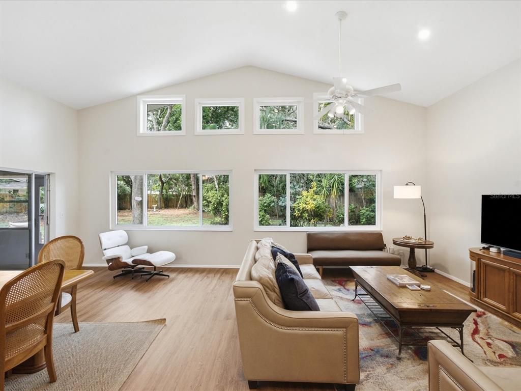A living room with vaulted ceilings, large windows, wood-look flooring, and a ceiling fan — 419 WAYFARER COURT, TARPON SPRINGS, FL