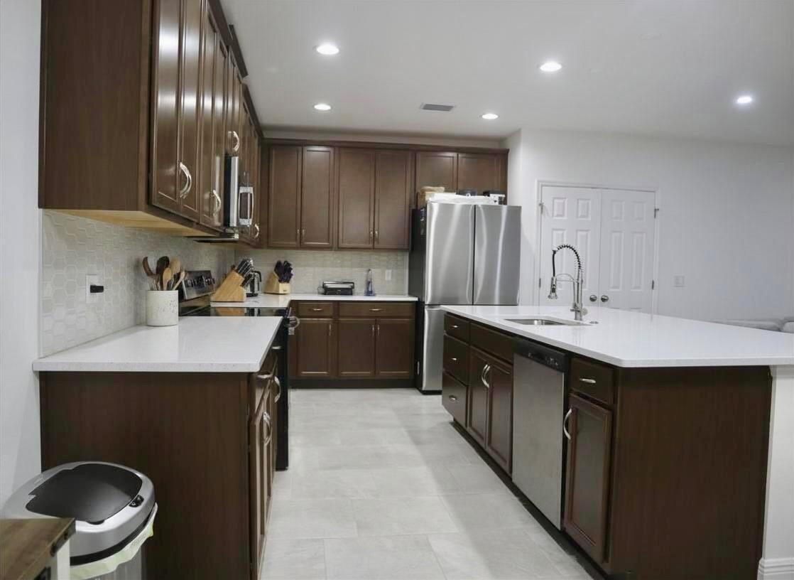 A kitchen features dark wood cabinets, white countertops, stainless steel appliances, and light tile flooring — 260 Hamlet Loop, Davenport FL 33837, DAVENPORT, FL