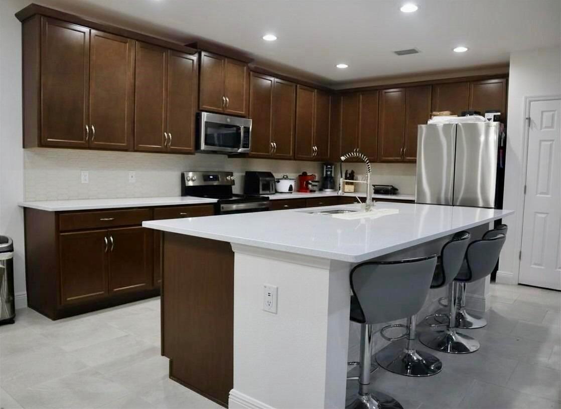 A kitchen features dark wood cabinets, white countertops, a central island with stools, and stainless-steel appliances — 260 Hamlet Loop, Davenport FL 33837, DAVENPORT, FL