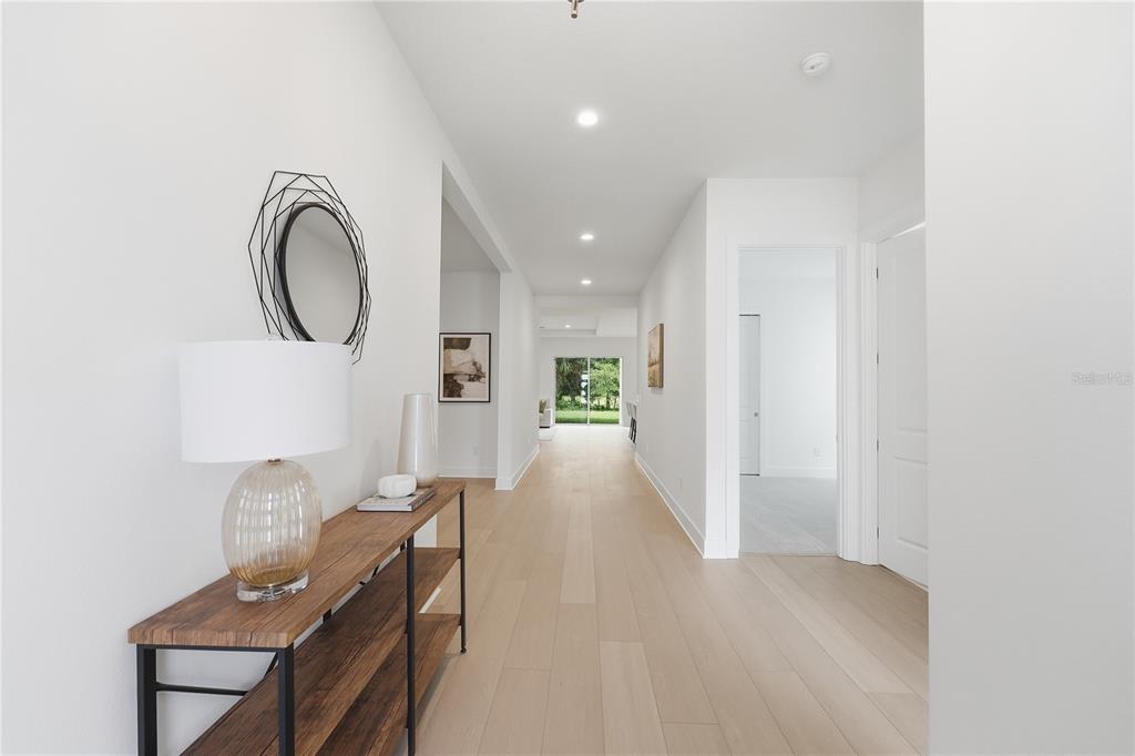 A bright hallway features light wood flooring, a console table, and a view toward outdoors — 1031 GLORYLAND COURT, SANFORD, FL