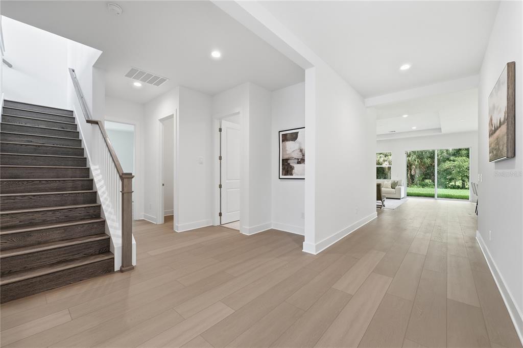 A bright entryway features a dark wood staircase, light hardwood floors, and white walls — 1031 GLORYLAND COURT, SANFORD, FL
