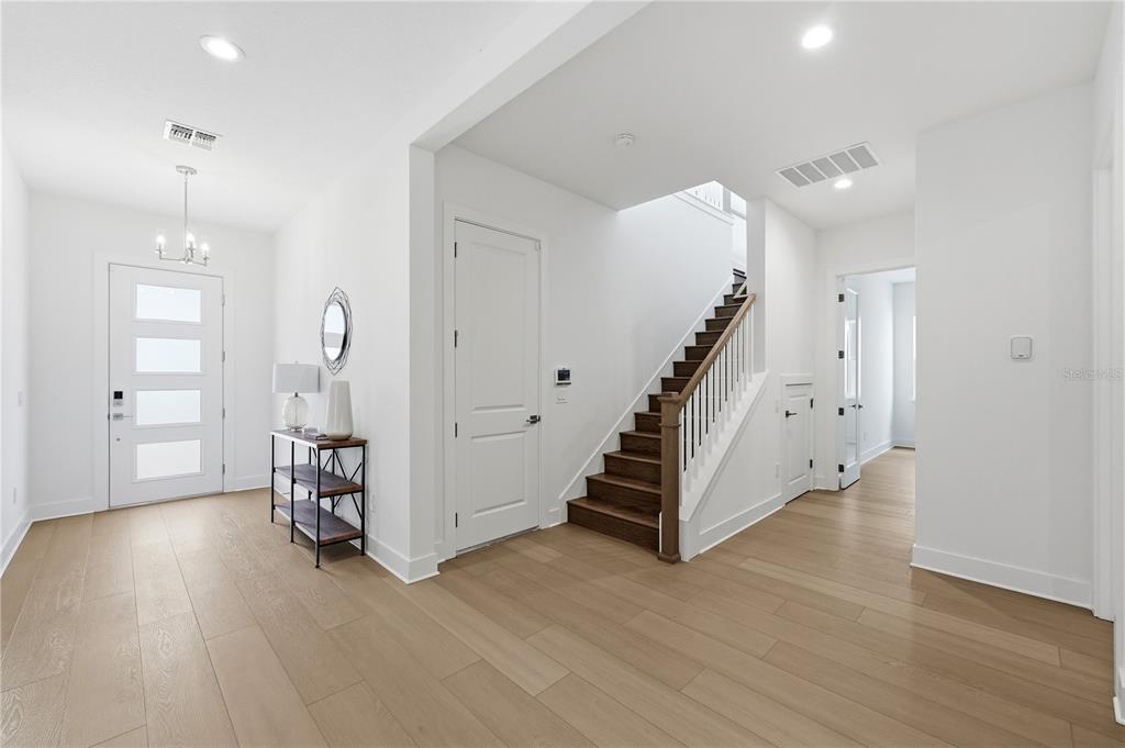 A bright entryway features light wood flooring, a white front door, and a wooden staircase — 1031 GLORYLAND COURT, SANFORD, FL