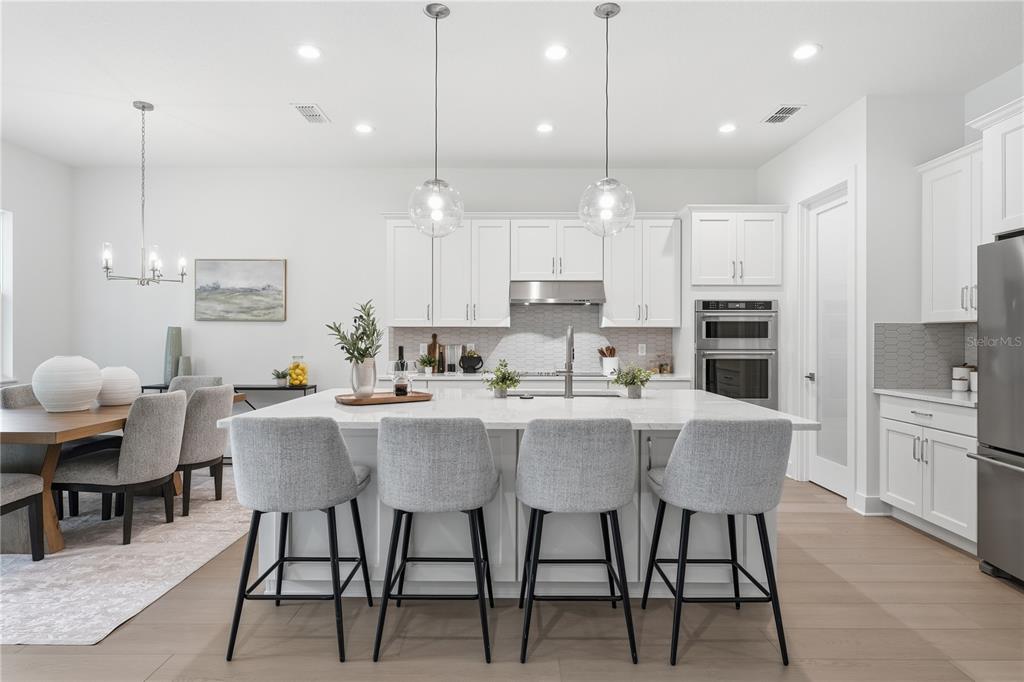 A modern kitchen features white cabinetry, a large island with four stools, and light flooring — 1031 GLORYLAND COURT, SANFORD, FL