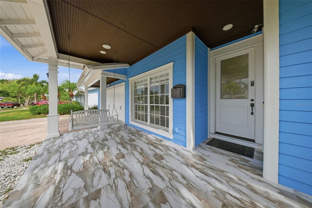 A blue-sided house features a covered porch with marble-look tile flooring and a white swing — 8722 PALISADES DRIVE, TAMPA, FL