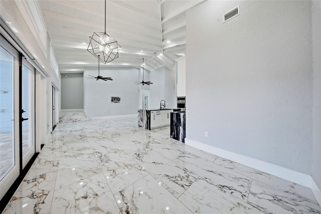 A bright, open-concept room features white marble-look tile flooring, vaulted ceilings, and a kitchen island — 8722 PALISADES DRIVE, TAMPA, FL