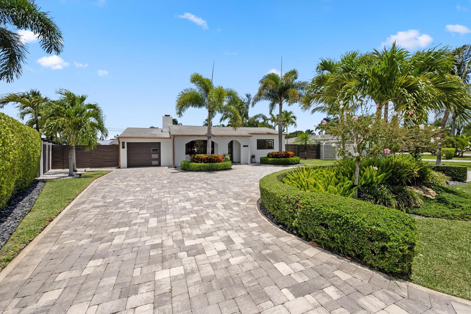 A single-story house with a paved driveway, palm trees, and manicured landscaping under a blue sky — 115 Highland Lane, Delray Beach FL 33444, DELRAY BEACH, FL