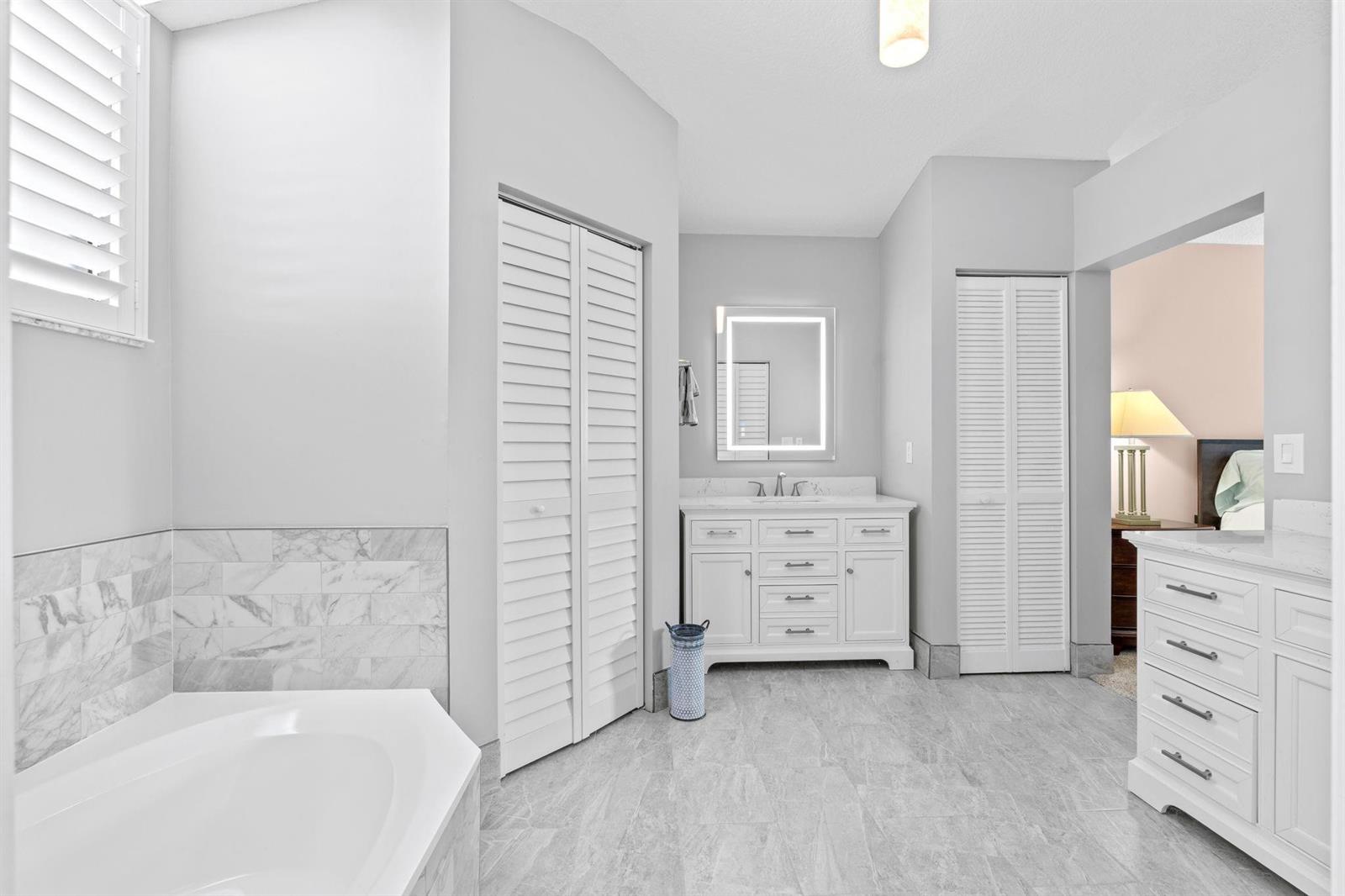 A bright bathroom features a soaking tub, white cabinetry, marble-look tile, and a vanity mirror — 8486 Heather Place, Boynton Beach FL 33472, BOYNTON BEACH, FL