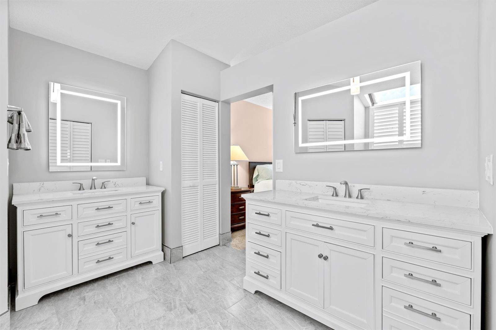 A bathroom with two white vanities, marble countertops, illuminated mirrors, and light gray tile flooring — 8486 Heather Place, Boynton Beach FL 33472, BOYNTON BEACH, FL