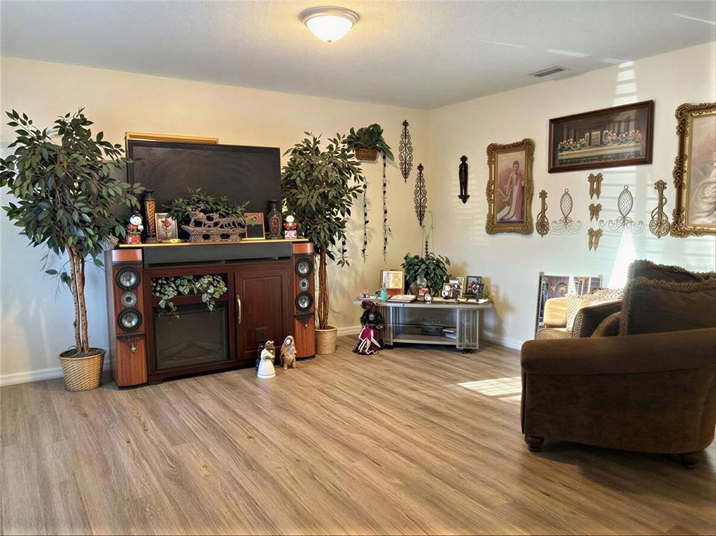 A living room features wood-look flooring, a fireplace media console, and decorative wall art — 4029 60TH STREET W, BRADENTON, FL