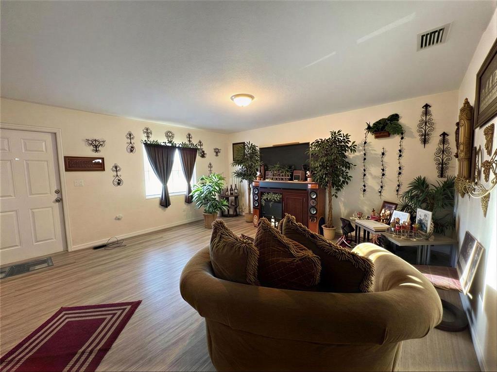 A living room features wood-look flooring, a large brown sofa, and several potted plants — 4029 60TH STREET W, BRADENTON, FL