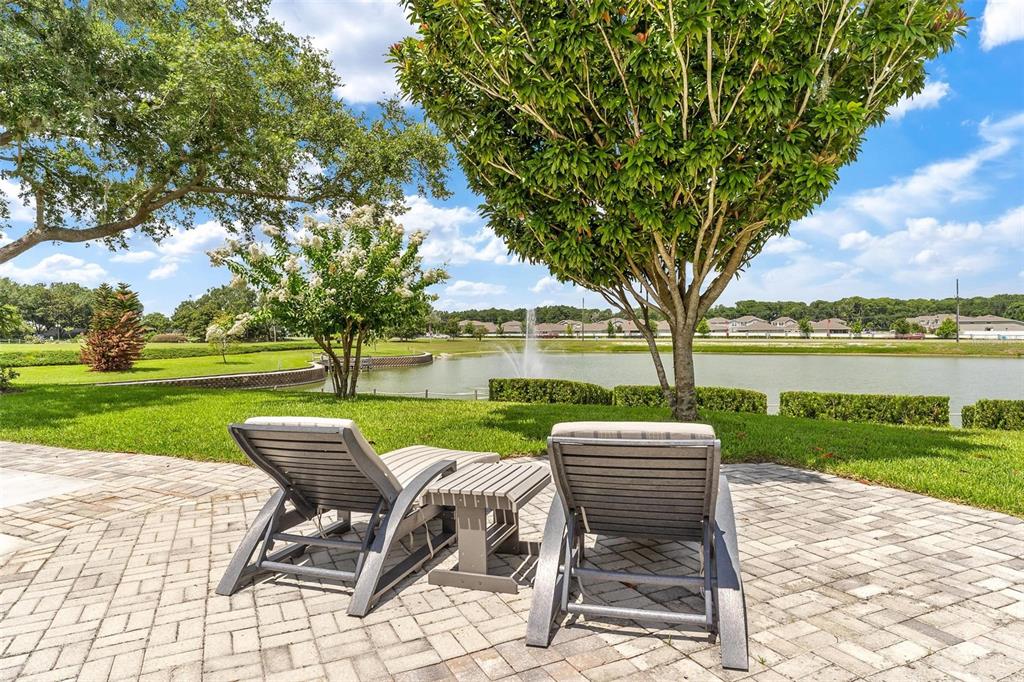 Two lounge chairs sit on a brick patio overlooking a pond with a fountain — 3354 SAINT LUCIA COURT, TAVARES, FL