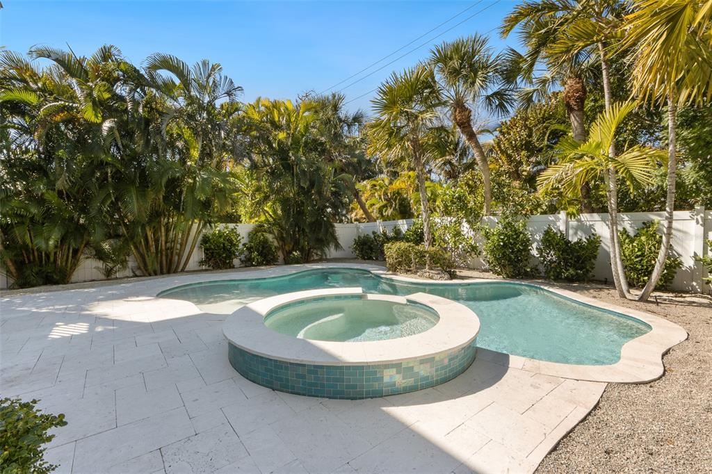 A backyard swimming pool with an integrated circular spa surrounded by light-colored stone pavers — 418 MAGNOLIA AVENUE, ANNA MARIA, FL