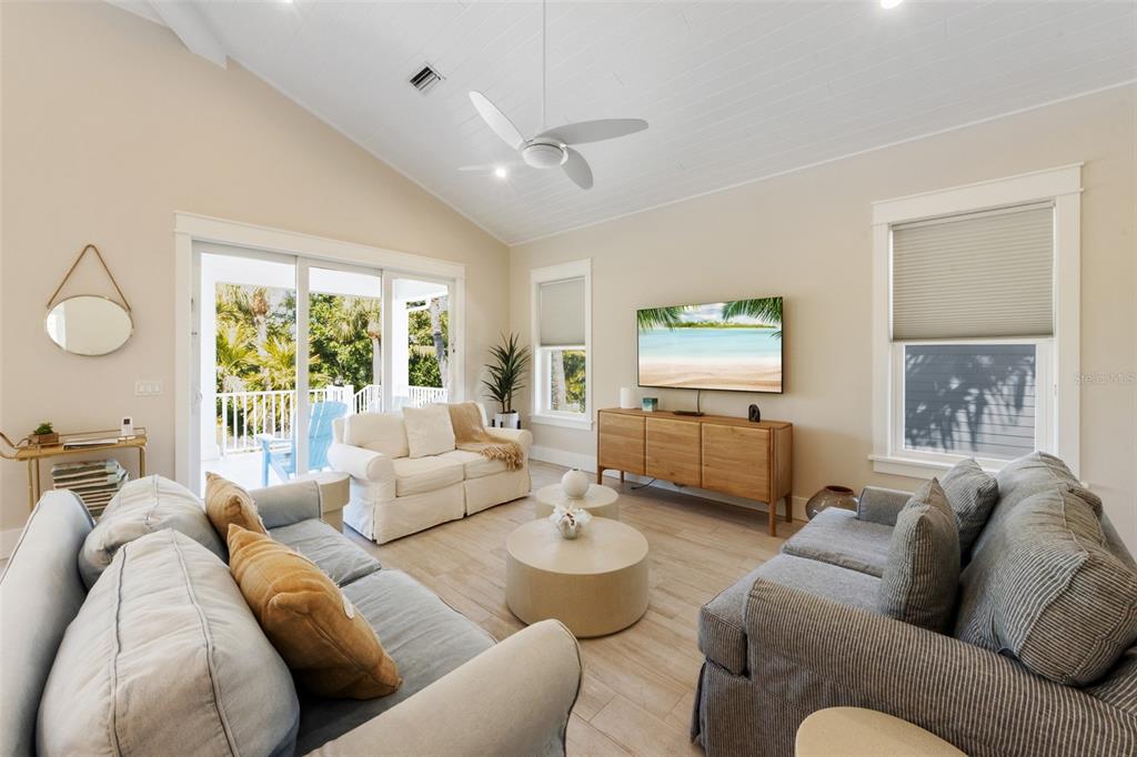 A living room features a vaulted ceiling, two sofas, a television, and a sliding glass door — 418 MAGNOLIA AVENUE, ANNA MARIA, FL