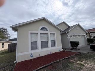 A single-story house with a beige stucco exterior, a front-facing garage, and a mulched garden bed — 114 VERVAIN AVENUE, DAVENPORT, FL