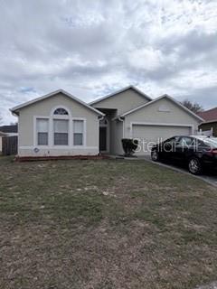 A single-story suburban house with a beige exterior, a two-car garage, and a front lawn — 114 VERVAIN AVENUE, DAVENPORT, FL