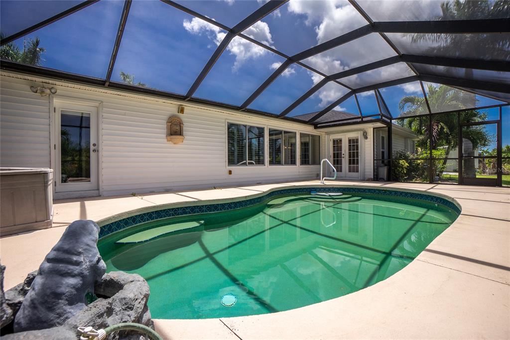 A screened-in swimming pool sits on a patio next to a white house — 14494 LILLIAN CIRCLE, PORT CHARLOTTE, FL