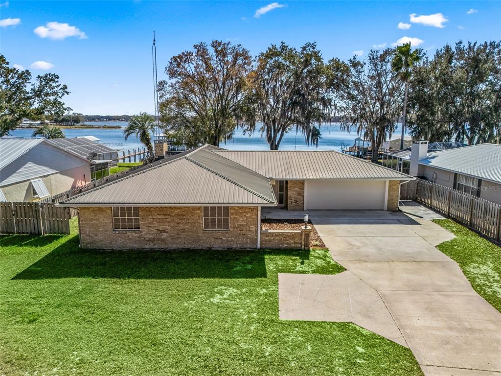 An aerial view of a single-story brick house with a metal roof and waterfront backyard — 10916 SE TIMUCUAN ROAD, SUMMERFIELD, FL