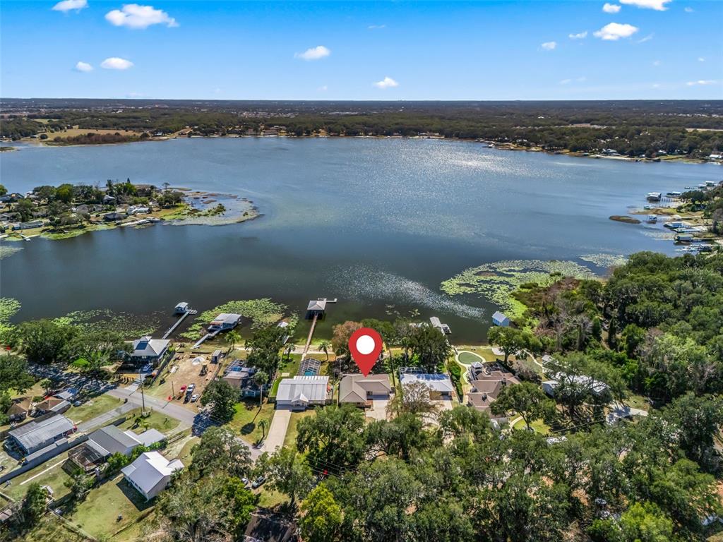 An aerial view shows a house with a red location pin beside a lake — 10916 SE TIMUCUAN ROAD, SUMMERFIELD, FL