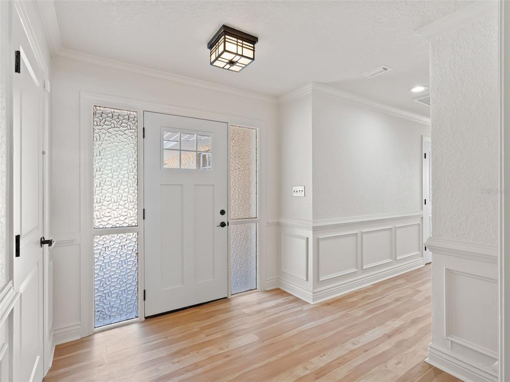 An entryway features a white front door with glass panels, wainscoting, and light wood flooring — 10916 SE TIMUCUAN ROAD, SUMMERFIELD, FL