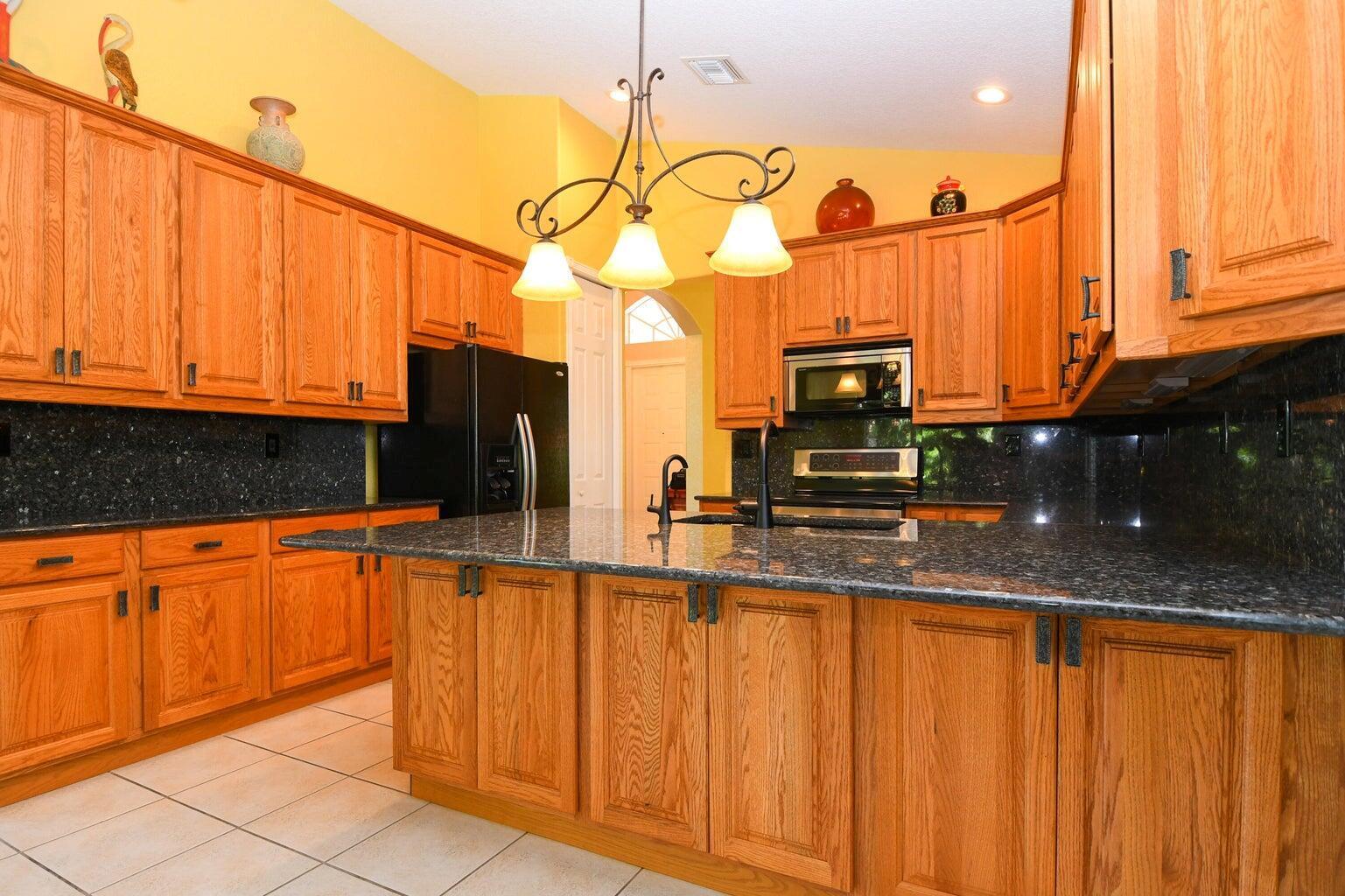 A kitchen with oak cabinets, dark granite countertops, a central island, and tile flooring — 8197 Cypress Point Road, West Palm Beach FL 33412, WEST PALM BEACH, FL
