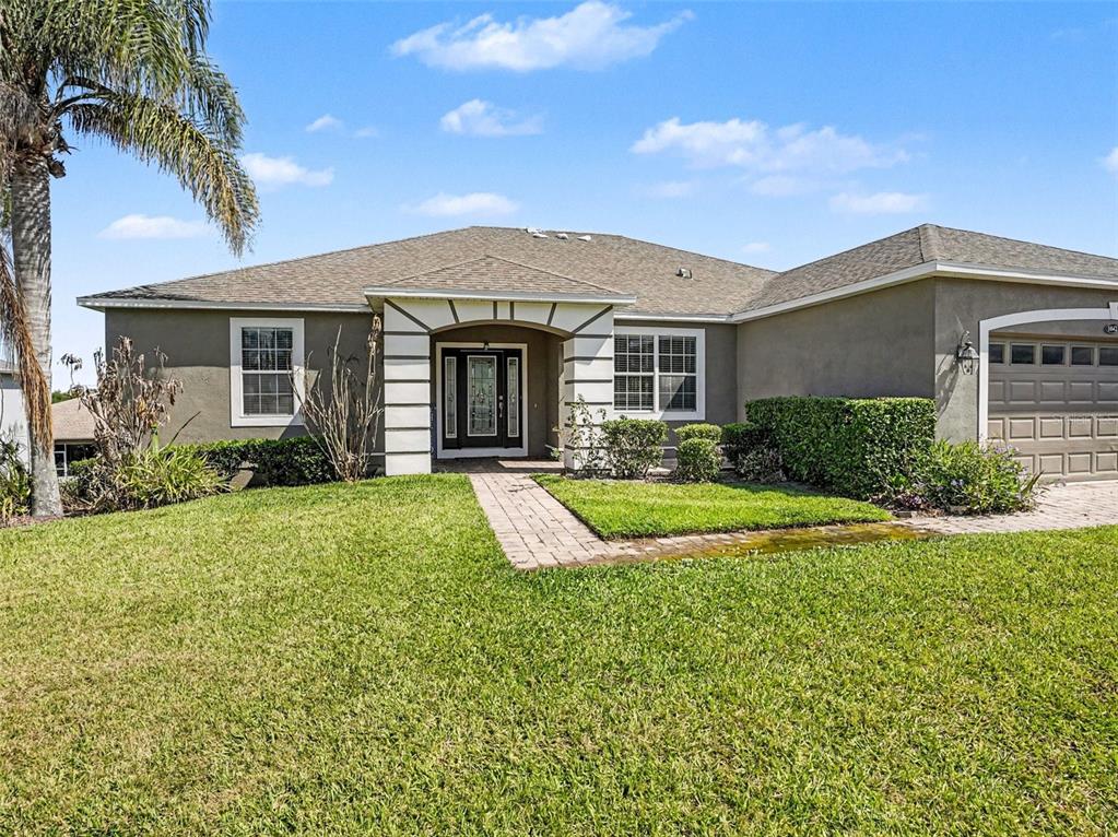 A single-story house with a tan stucco exterior, a paved walkway, and a two-car garage — 1042 HARMONY LANE, CLERMONT, FL